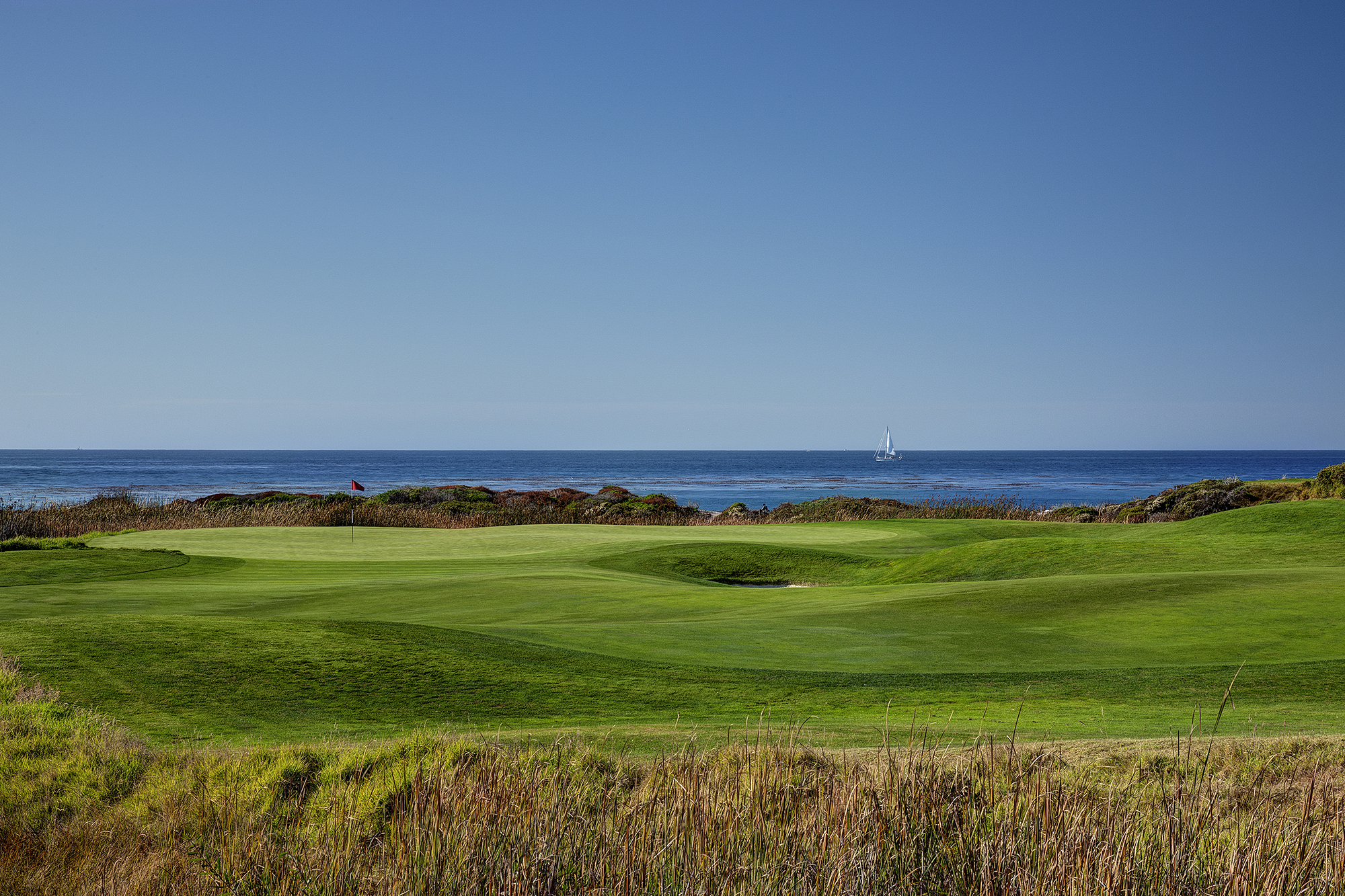 The 7th green at The Links of Spanish Bay with the Pacific Ocean and a sail boat in the background