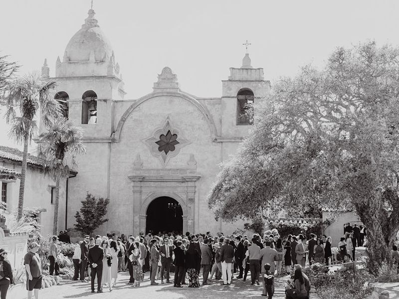 Black and white photo of church with wedding attendees outside