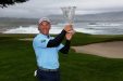 Scott McCarron standing on a golf course, wearing a blue shirt holding a crystal trophy with the ocean behind him.