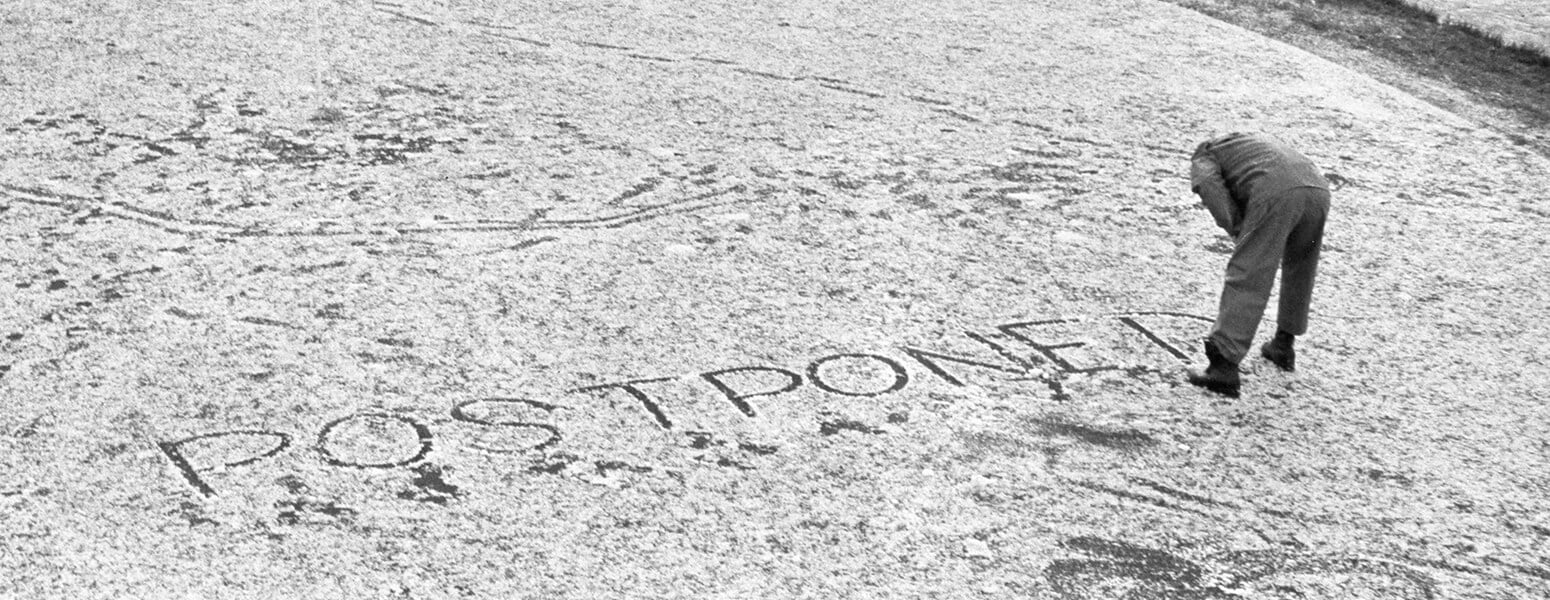 Black and white image showing golfer writing the word postpone in the snow